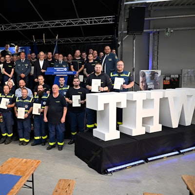 THWler stehen  mit Urkunden und Medaillen hinter einem großen weißen Schriftzug „THW“.