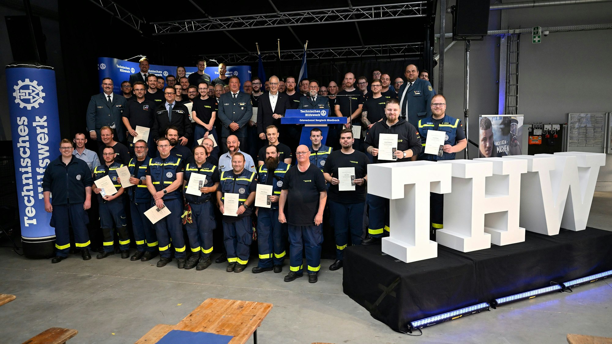 THWler stehen  mit Urkunden und Medaillen hinter einem großen weißen Schriftzug „THW“.