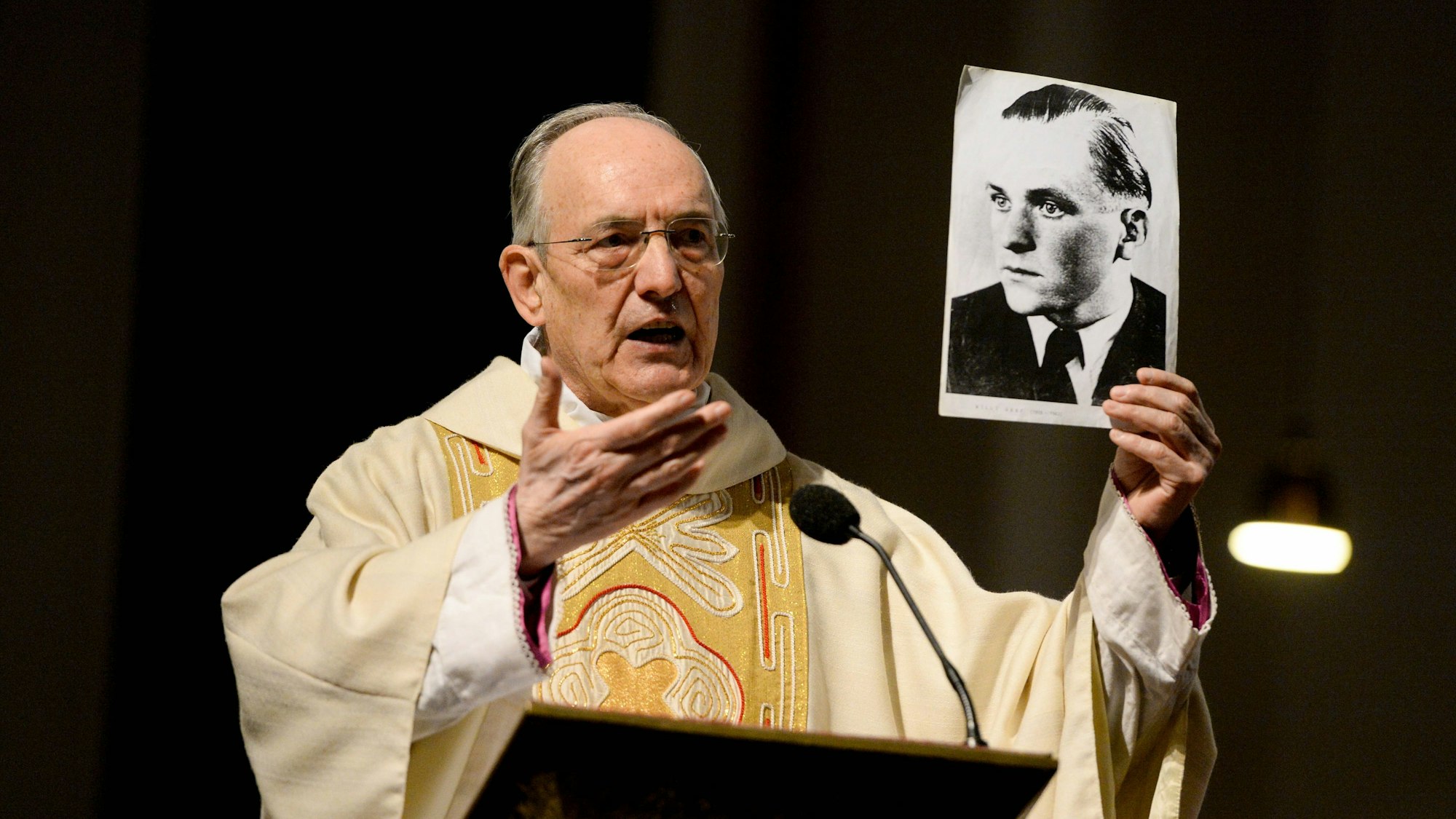 Prälat Prof. Dr. Helmut Moll 2013 im Priestergewand. Er hält ein Foto von Willi Graf in der Hand.
