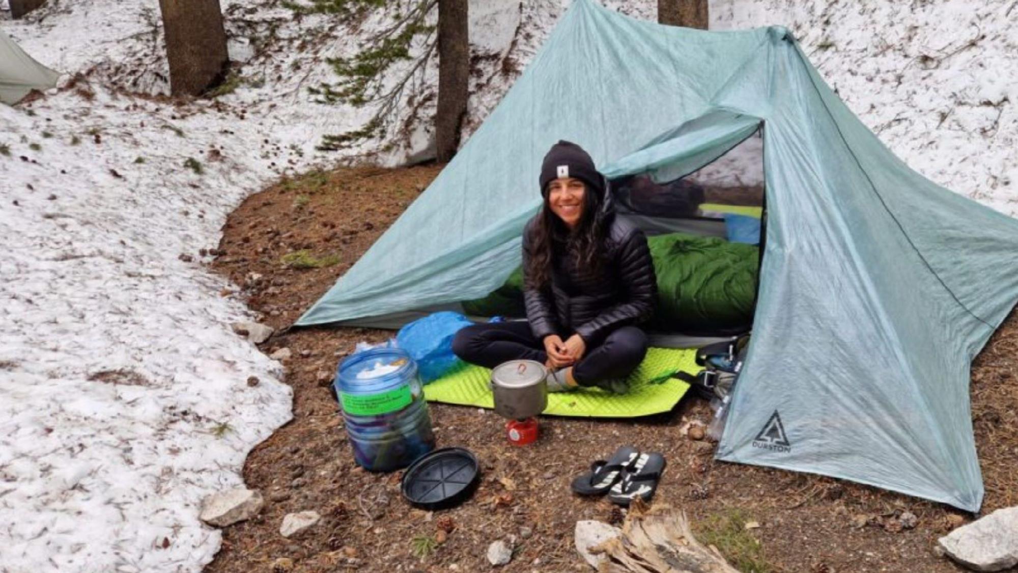 Miriam Wiesner sitzt vor einem Zelt im Schnee. Vor sich ein Trecking-Kocher.
