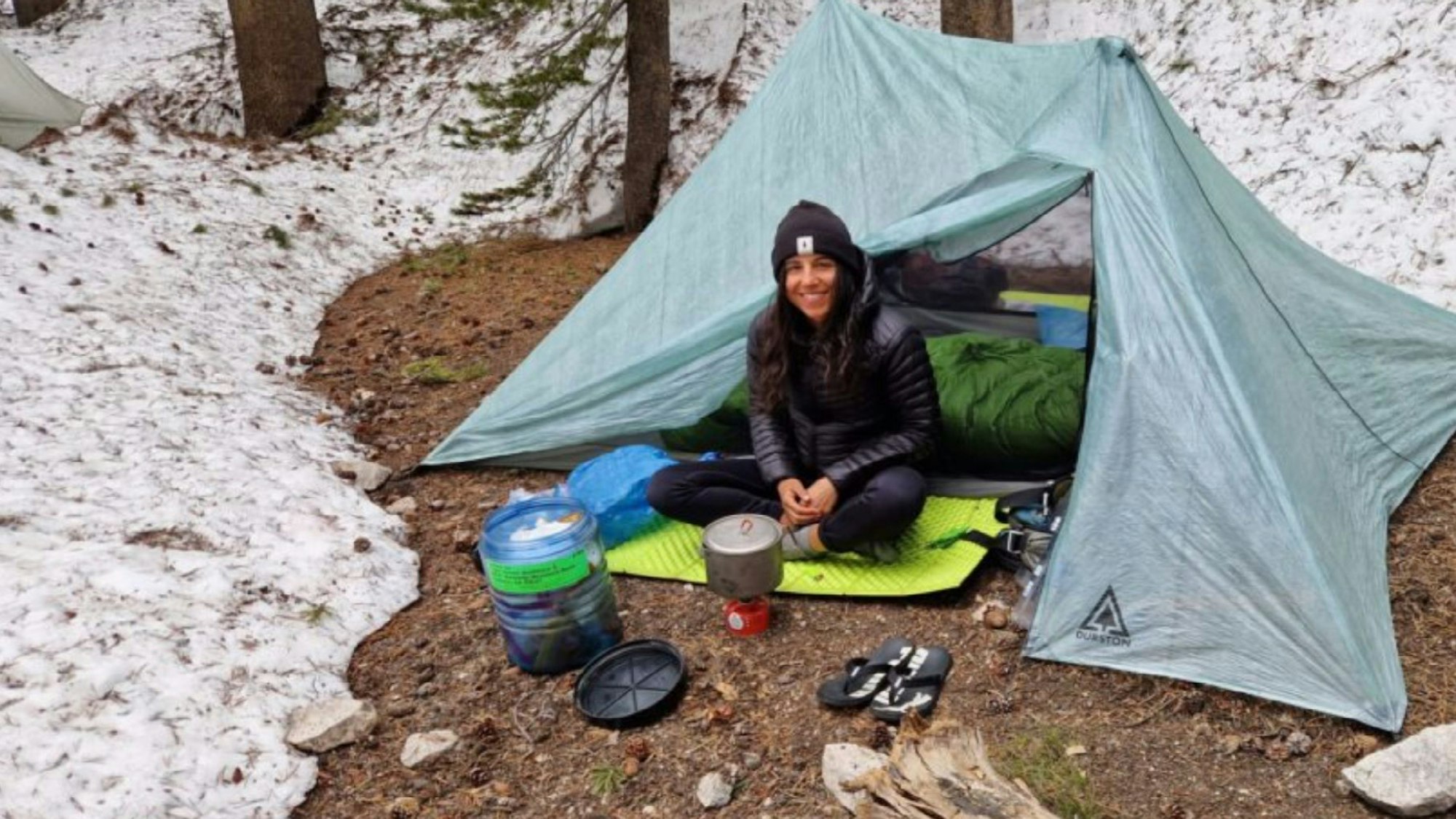 Miriam Wiesner sitzt vor einem Zelt im Schnee. Vor sich ein Trecking-Kocher.