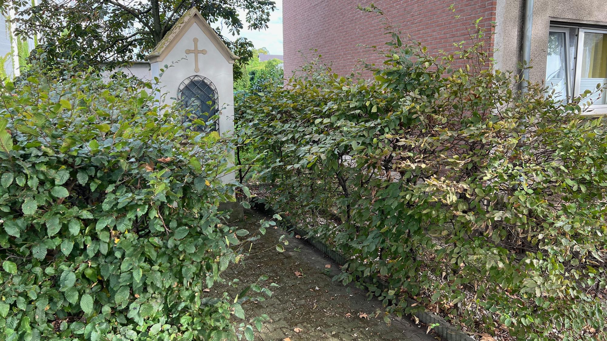 Das Bild zeigt ein Heiligen-Häuschen hinter einer Hecke.