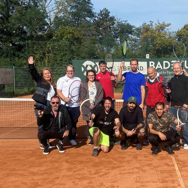 Eine Gruppe Menschen posiert in Sportkleidung und mit Tennisschlägern vor einem Tennisnetz.