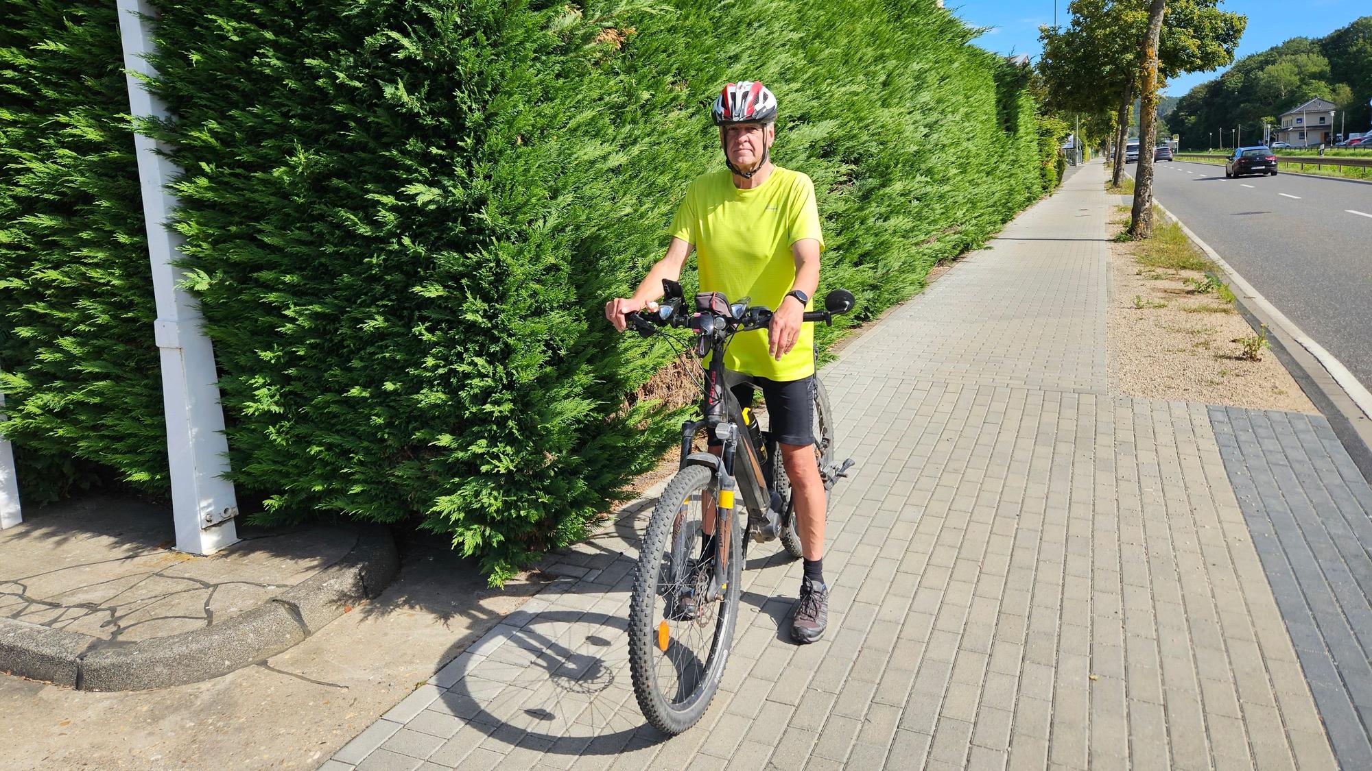 Wolfgang Röhrich ist mit seinem Fahrrad auf dem Radweg an der Bundesstraße in Gemünd unterwegs. Er hat an einer gefährlichen Einfahrt an einer Hecke angehalten.