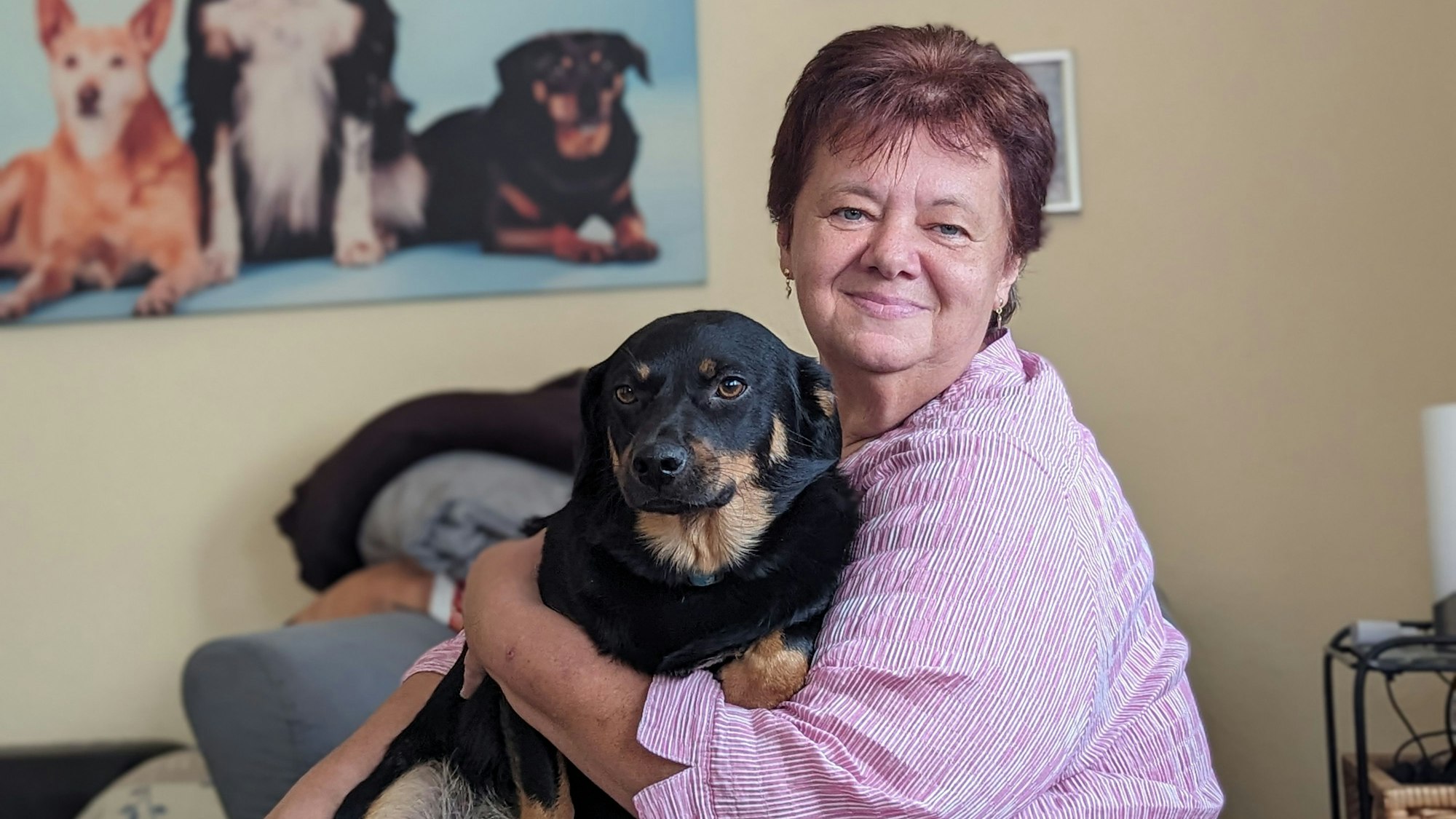 Eine Frau mit ihrem Hund in ihrem Wohnzimmer vor einem Hundefoto.