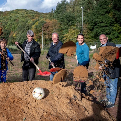 Das Bild zeigt den offiziellen Spatenstich. Die Beteiligten werfen Sand mithilfe von Schaufeln in Richtung Kamera.