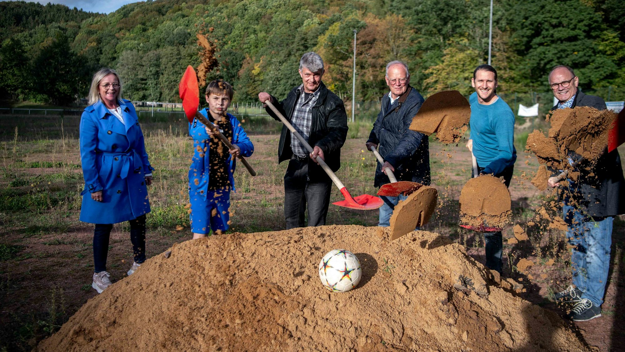 Das Bild zeigt den offiziellen Spatenstich. Die Beteiligten werfen Sand mithilfe von Schaufeln in Richtung Kamera.