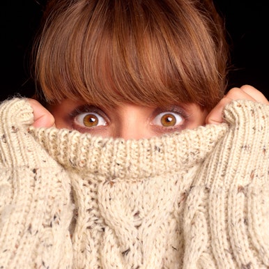 Junge Frau verkriecht sich in bis über die Nase in ihrem Pullover