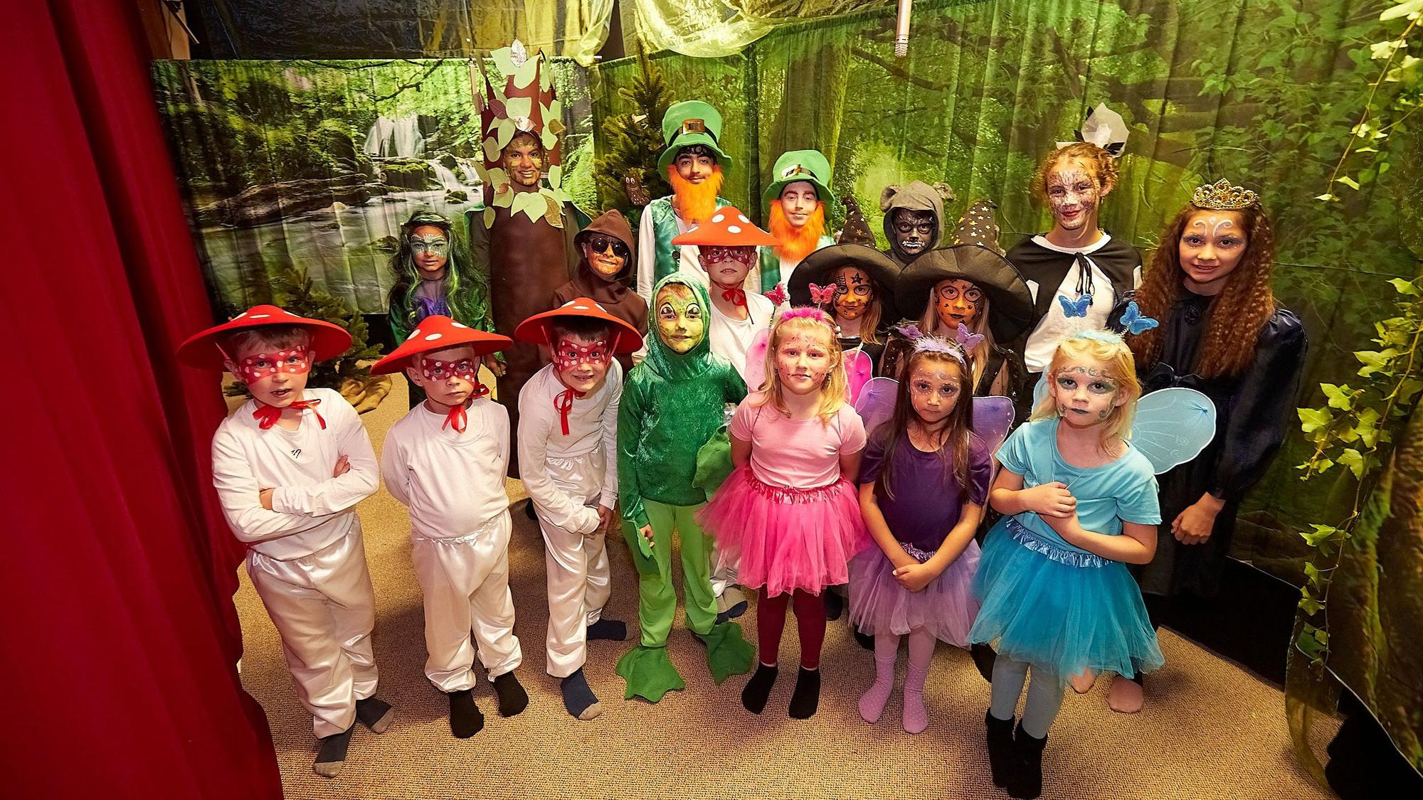 Die Kinder des Theatervereins Nettersheim stehen in ihren Kostümen auf der Theaterbühne, die eine Wald-Kulisse zeigt.