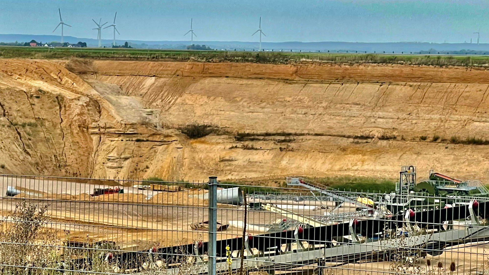 Blick in eine Kiesgrube mit Windrädern im Hintergrund.