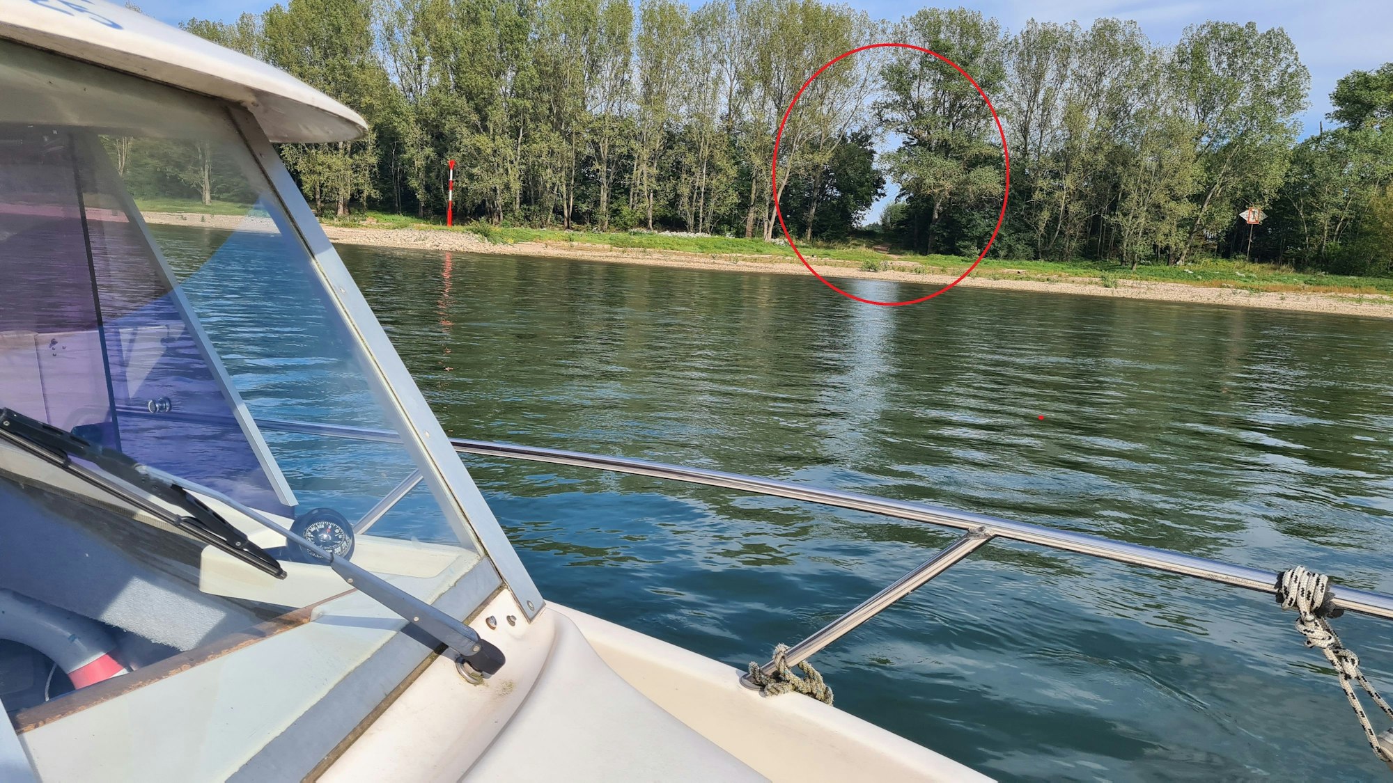 Vom Boot aus fotografiert ist ein Teil des Boots, der Rhein und eine Schneise am Ufer zu sehen.
