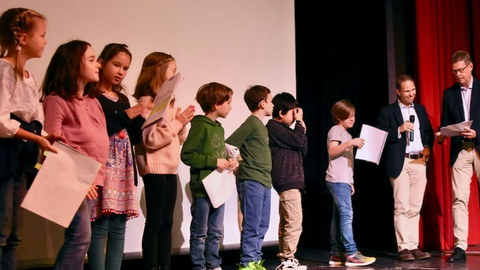 Kinder und zwei Männer stehen auf einer Bühne