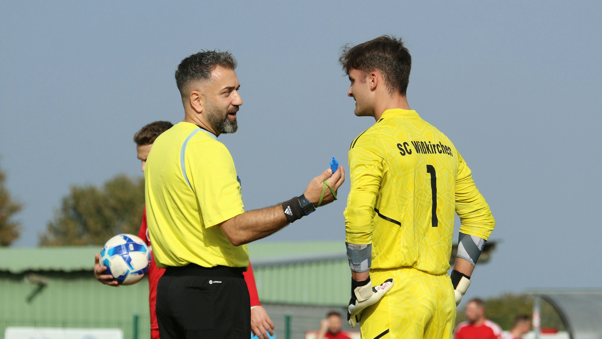 Ein Schiedsrichter und ein Torwart unterhalten sich. Beide lächeln.