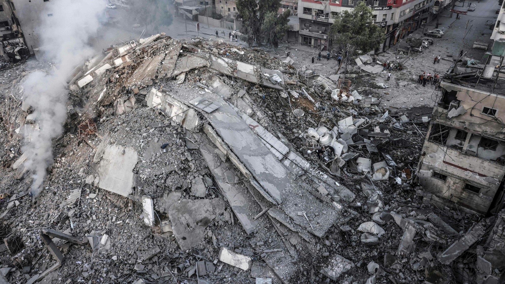 TOPSHOT - People walk around the ruins of a building destroyed in Israeli airstrikes in Gaza City on October 8, 2023. Fighting between Israeli forces and the Palestinian militant group Hamas raged on October 8, with hundreds killed on both sides after a surprise attack on Israel prompted Prime Minister Benjamin Netanyahu to warn they were "embarking on a long and difficult war". (Photo by Mohammed ABED / AFP)