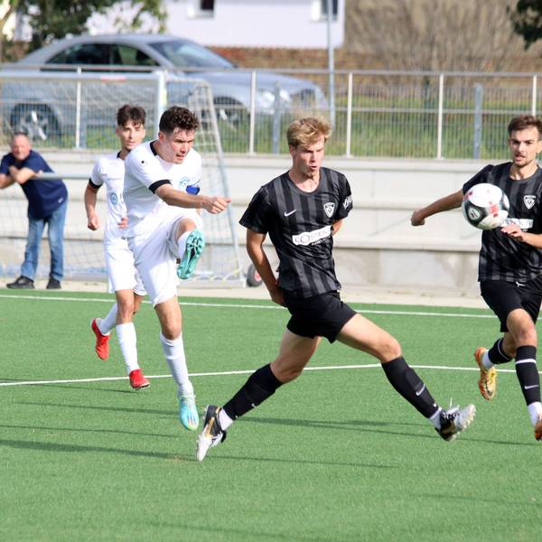 Ein Fußballspieler schießt zwischen zwei Verteidigern hindurch. Einer von ihnen dreht dem Schützen den Rücken zu.