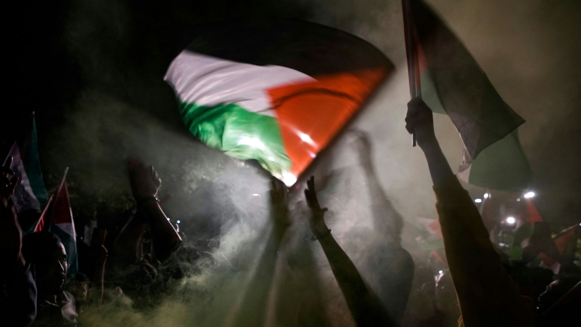 Menschen skandieren israelfeindliche Parolen und schwenken palästinensische Fahnen.