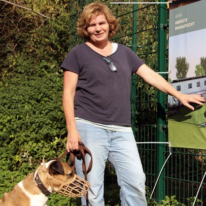Eine Frau mit einem Hund an der Leine zeigt auf ein Banner.