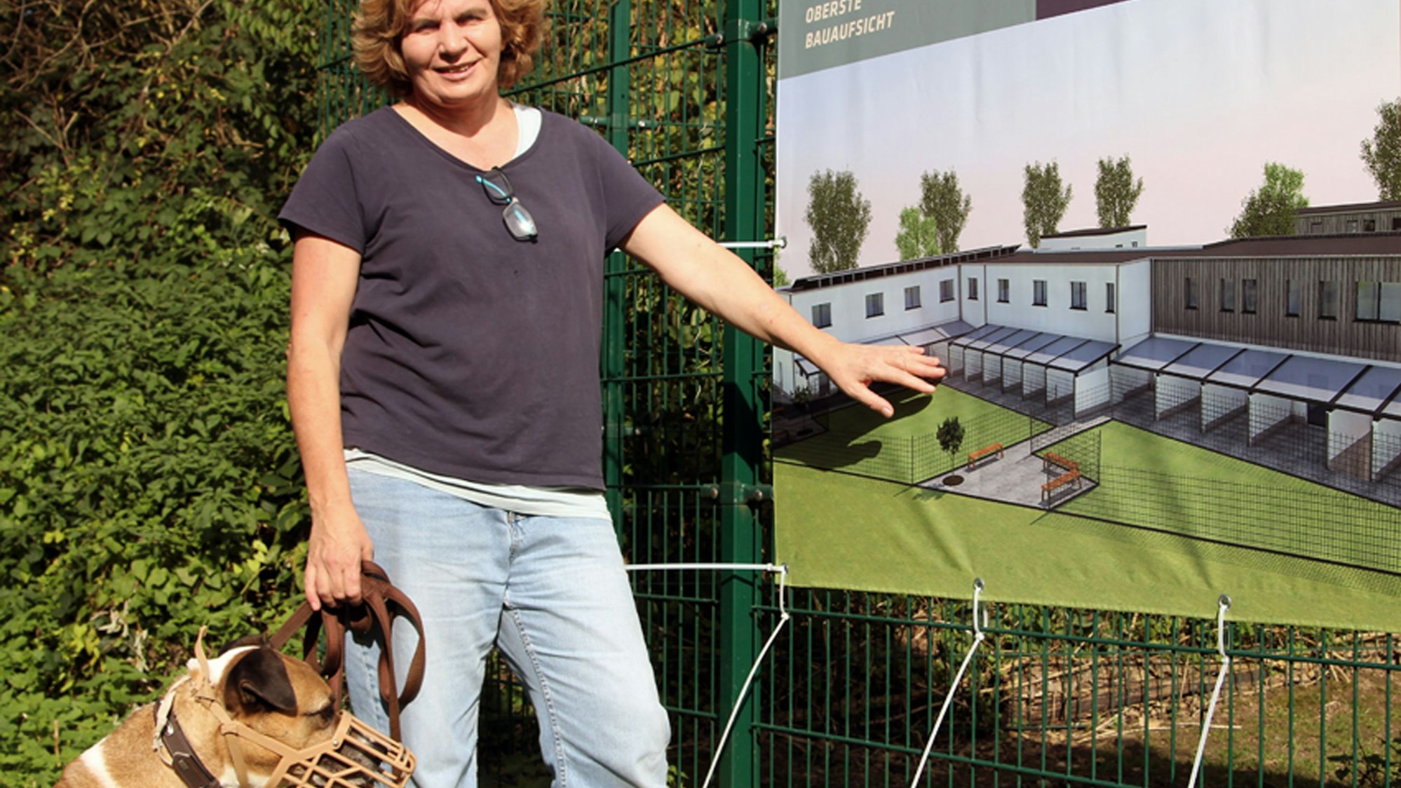 Eine Frau mit einem Hund an der Leine zeigt auf ein Banner.