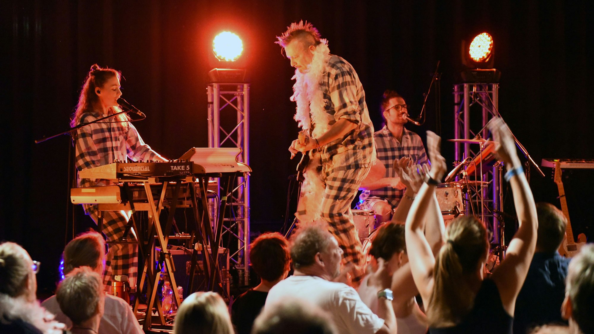 Eine Band, bestehend aus einem Gitarristen, einer Keyboarderin und einem Schlagzeuger spielen auf einer Bühne.