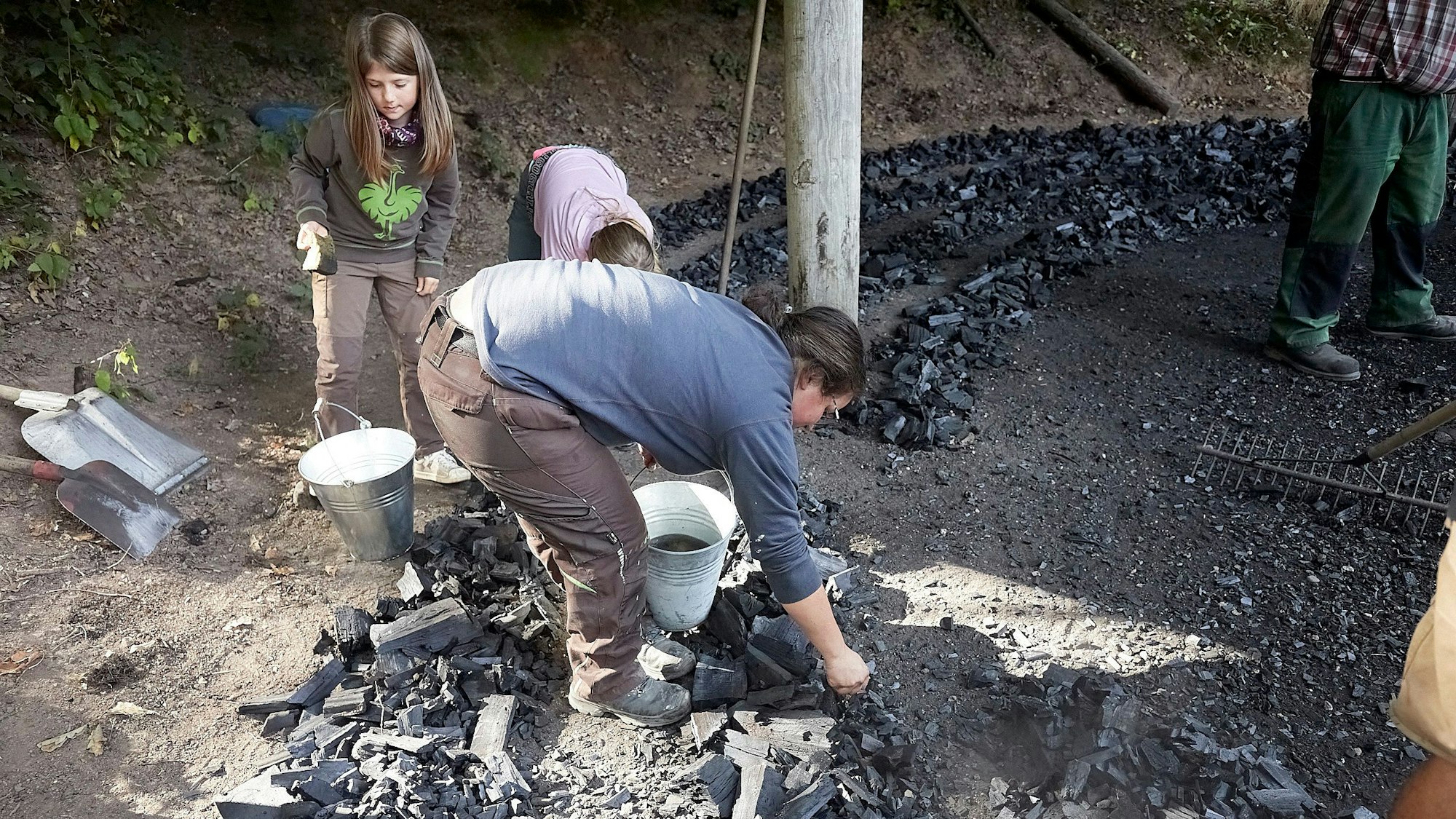 Zwei Kinder und eine Frau sammeln Kohle auf.