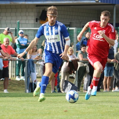 Vor vollen Rängen führen zwei Fußballer ein Laufduell.