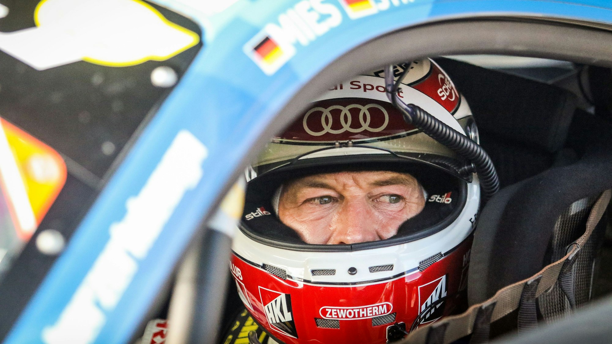 Frank Stippler hat das Visier seines Helmes hoch geklappt und blickt aus dem Seitenfenster seines Rennwagens.