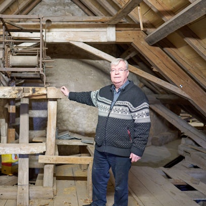 Helmut J. Kirfel steht vor einem Holzgerüst, auf der die Reste einer Uhr aus dem 15. Jahrhundert auf dem Dachboden der Steinfelder Basilika zu sehen sind.