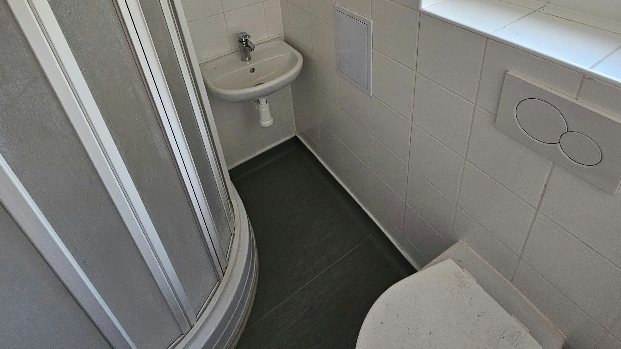 Zu sehen ist ein Waschbecken, eine Dusche und eine Toilette.