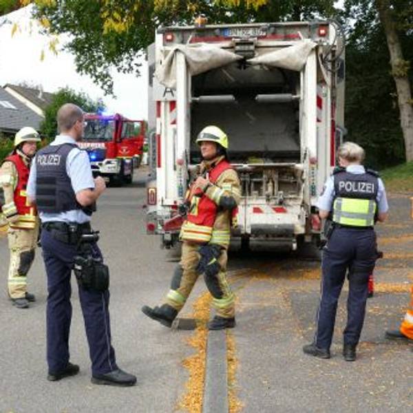 Feuerwehrleute und Polizeibeamte hinter dem Müllwagen.