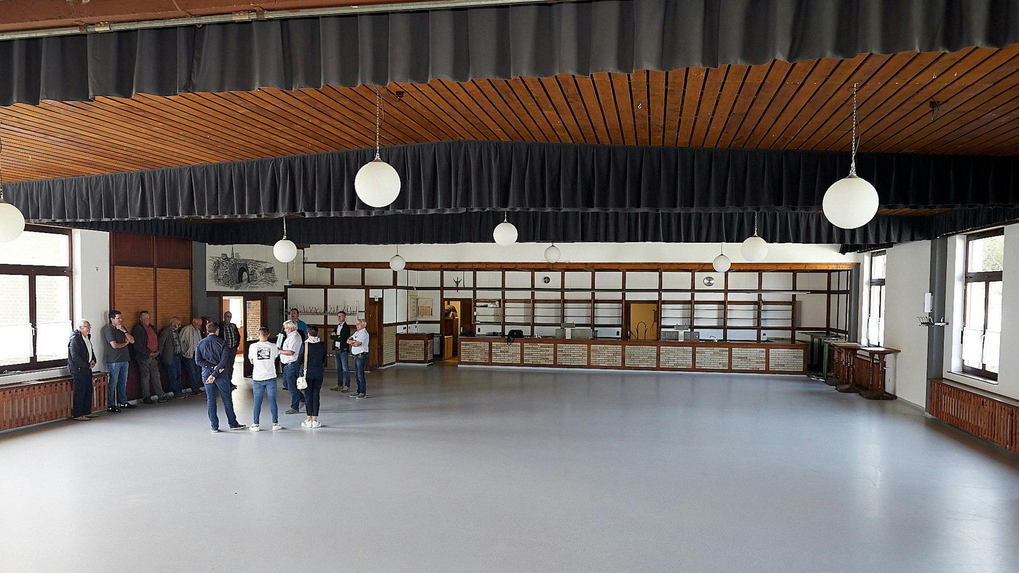 Das Bürgerhaus in Schmidtheim hat einen neuen Boden und eine neue Decke. Im Hintergrund steht eine Gruppe Menschen und betrachtet die neuen Elemente.
