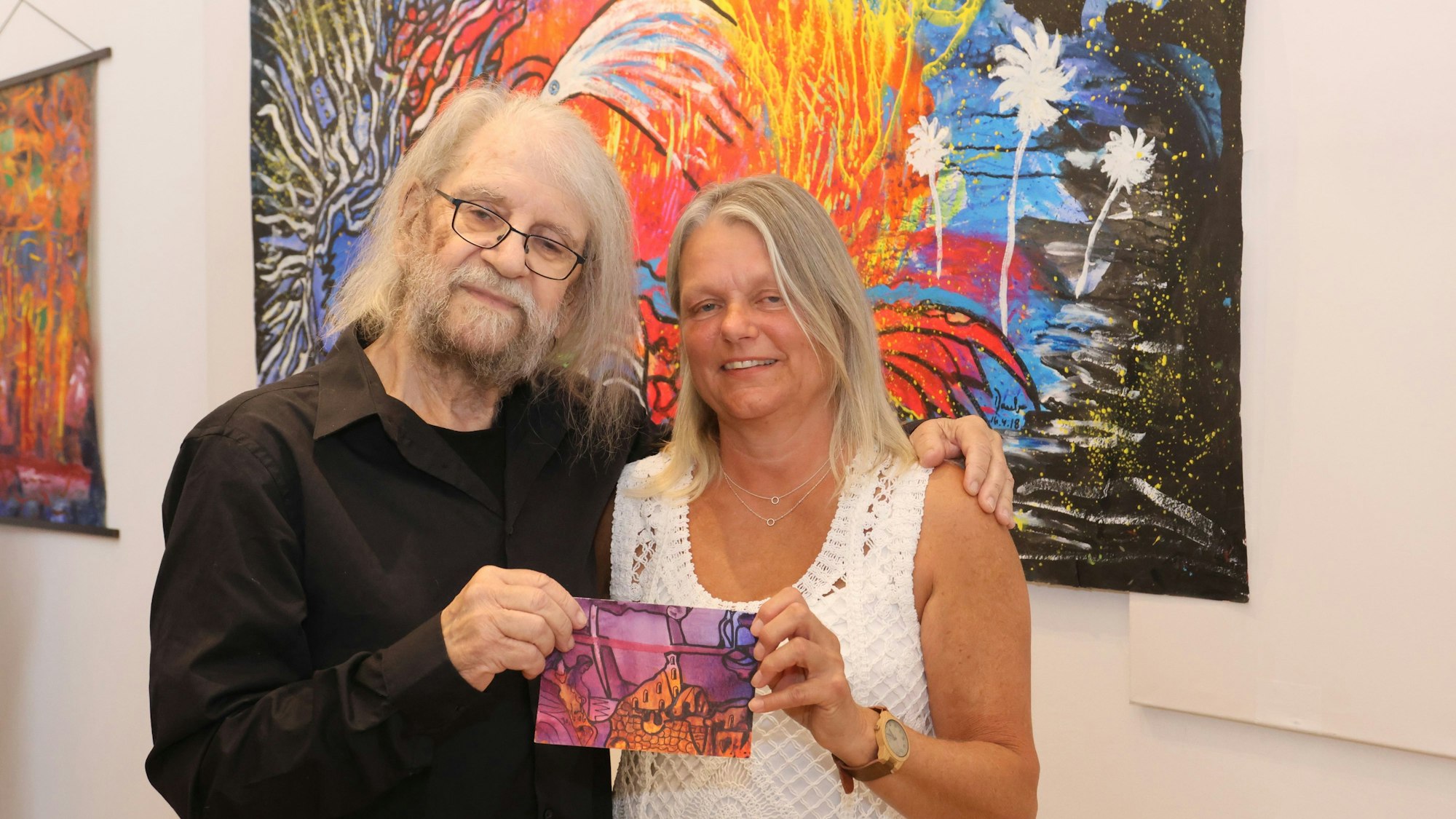 Eugen Daub und seine ehemalige Schülerin Silvia Kallabi stehen vor einem von Daubs bunten Gemälden.