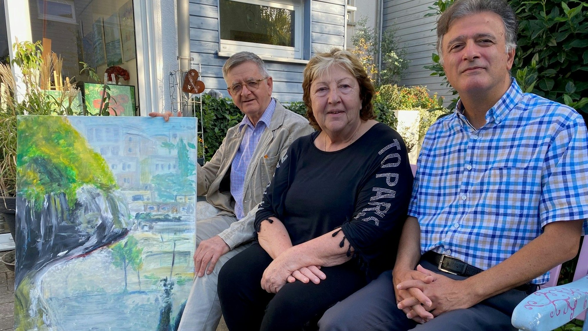 Zu sehen sind die drei Mitglieder des Arbeitskreises Palästina Brühl-Battir sowie ein Gemälde, das den Ort im Westjordanland zeigt.