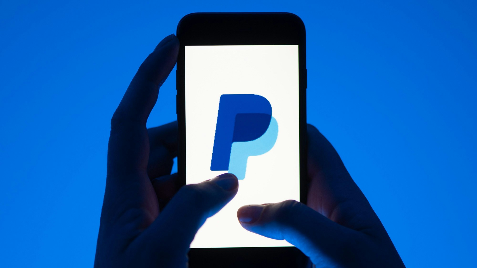 Eine Frau hält ein Smartphone mit dem Logo des Bezahldienstes Paypal.