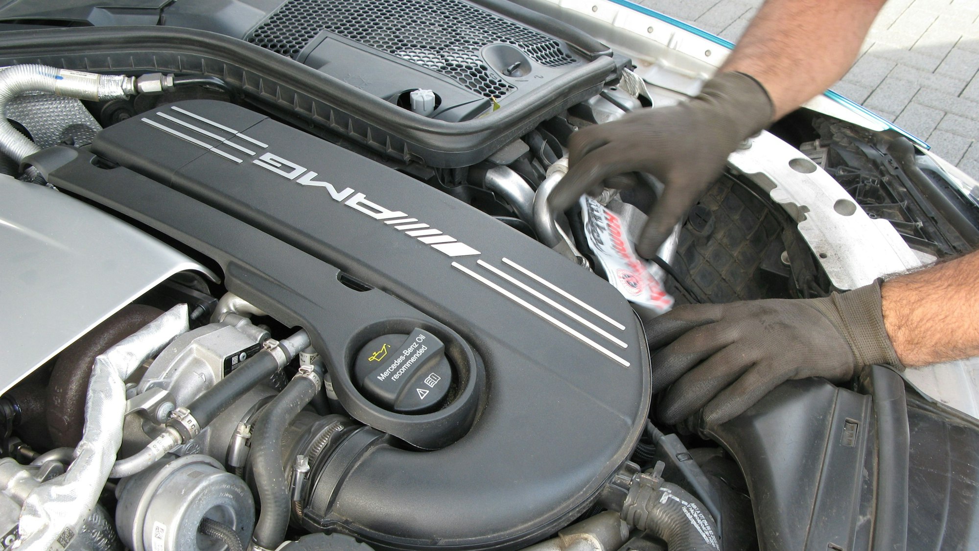 Mit Händen in dunkelgrauen Handschuhen arbeitet ein Mann an einem Automotor.