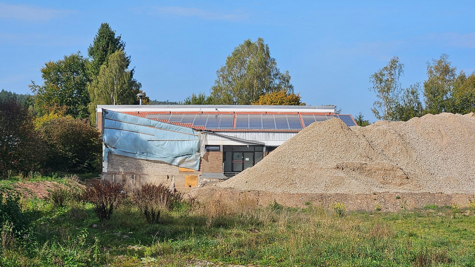 Die Turnhalle der ehemaligen Grundschule ist zum Teil durch einen Haufen mit Steinen verdeckt.