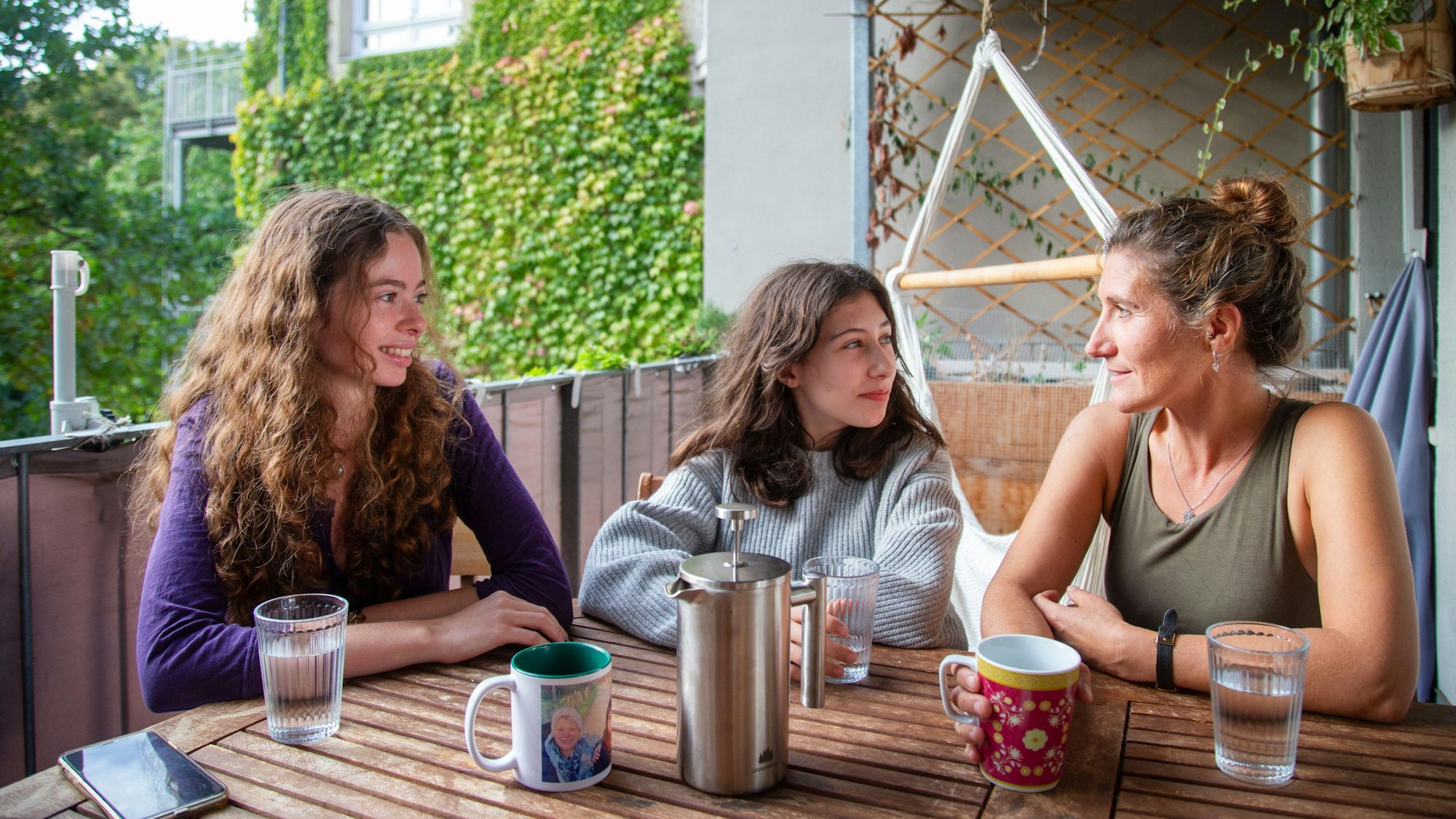 Nourhan El Kouche, Clara Panne und Christina Panne (v.l.) sitzen auf dem Balkon und trinken Kaffee.