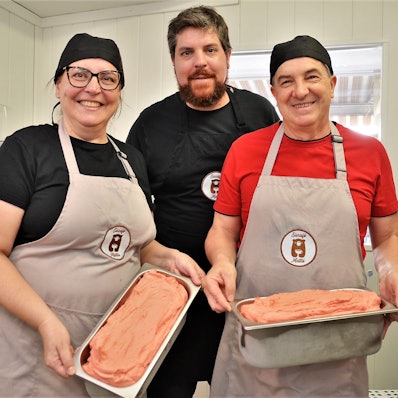 Rafael Matté (Mitte), sein Vater André und seine Mutter Fernanda stehen zusammen in der Waldbröler Eisküche und halten zwei große Schalen mit Eiscreme in den Händen.