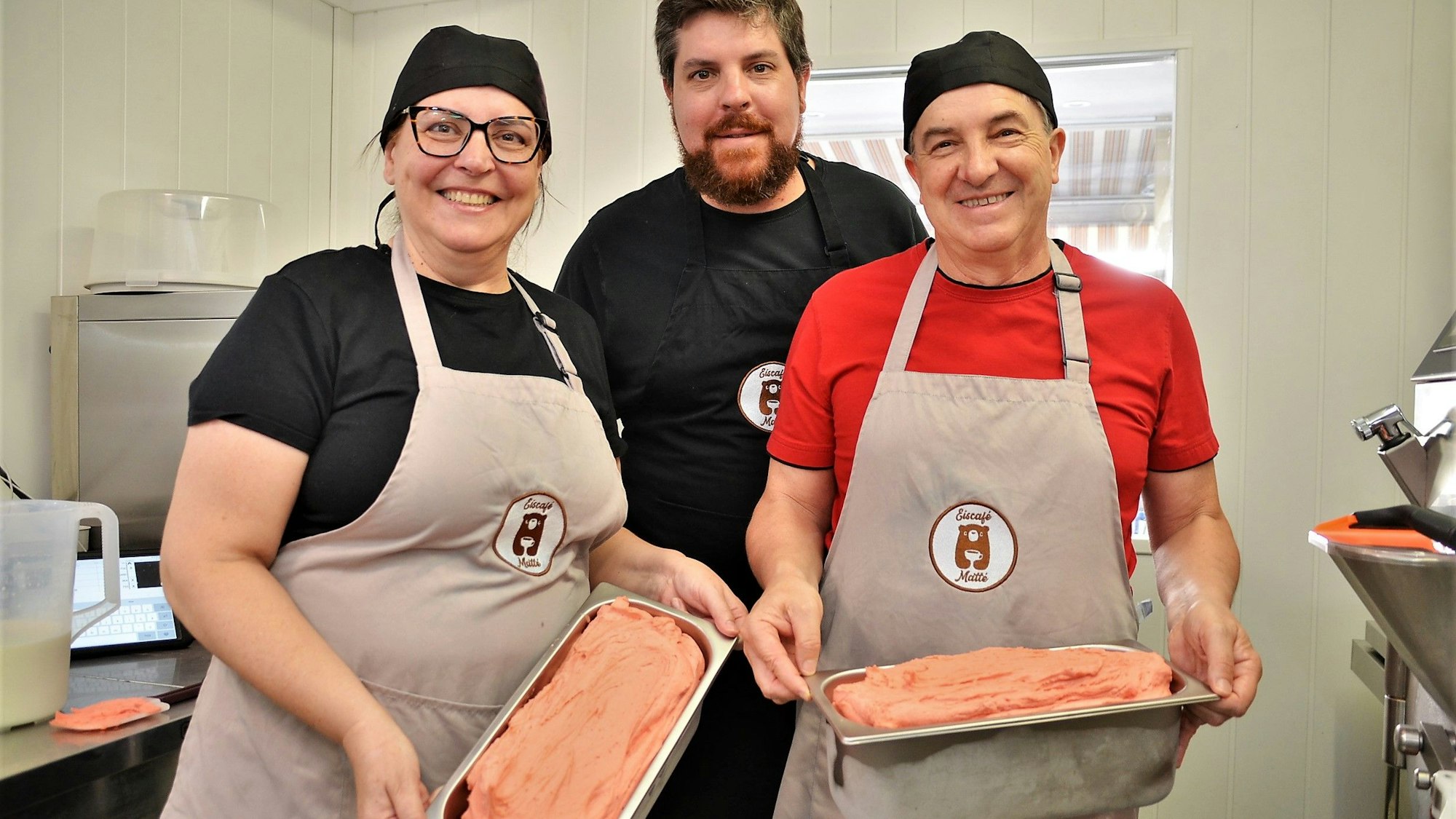 Rafael Matté (Mitte), sein Vater André und seine Mutter Fernanda stehen zusammen in der Waldbröler Eisküche und halten zwei große Schalen mit Eiscreme in den Händen.