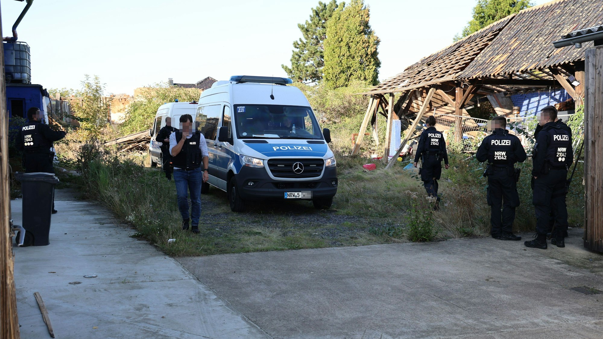 Zwei Transporter der Polizei sind aufs Grundstück gefahren. Polizisten stehen bereit für die Durchsuchung.