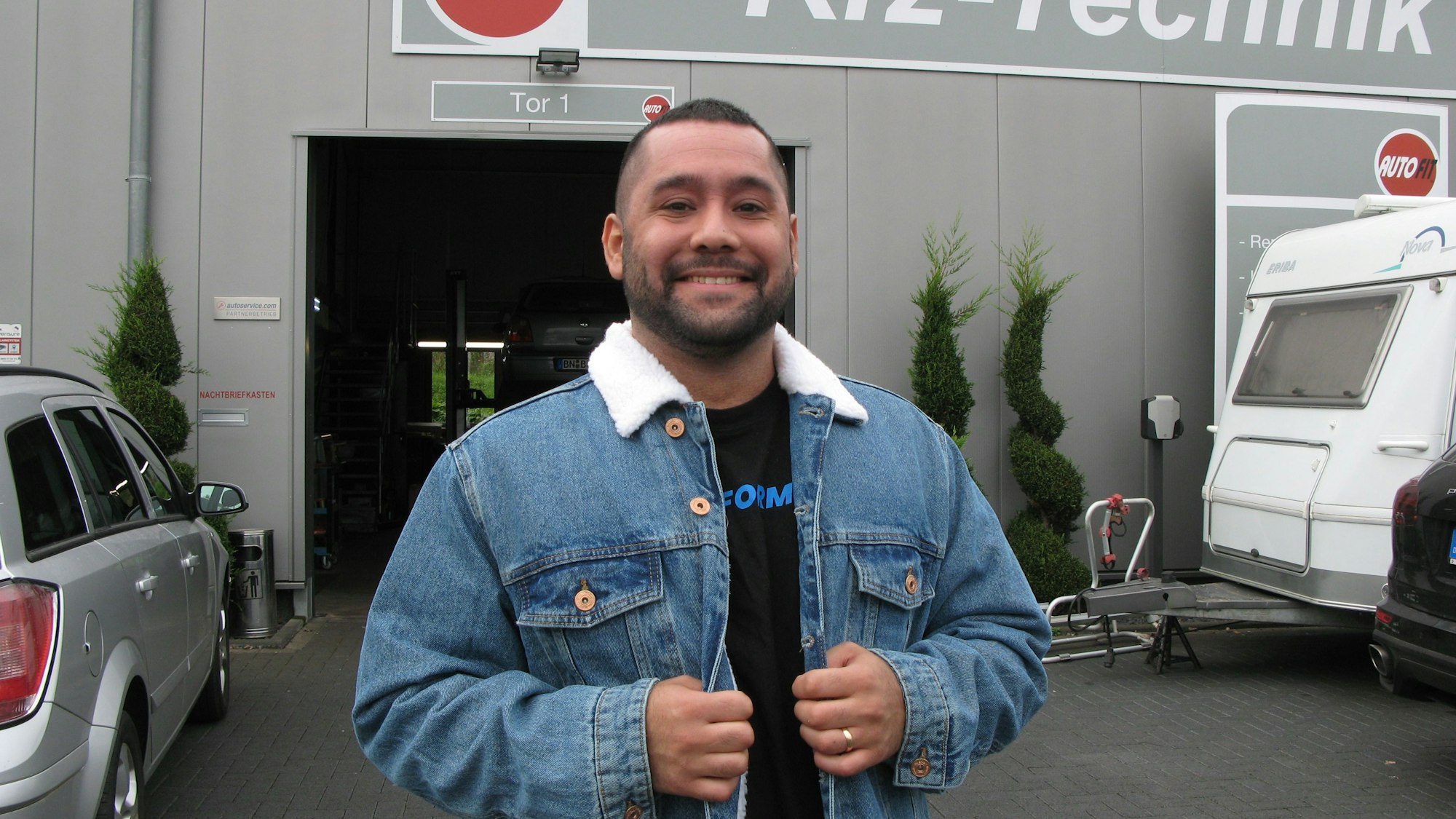 Der 29-jährige Pourya Jalali steht vor einer Autowerkstatt.