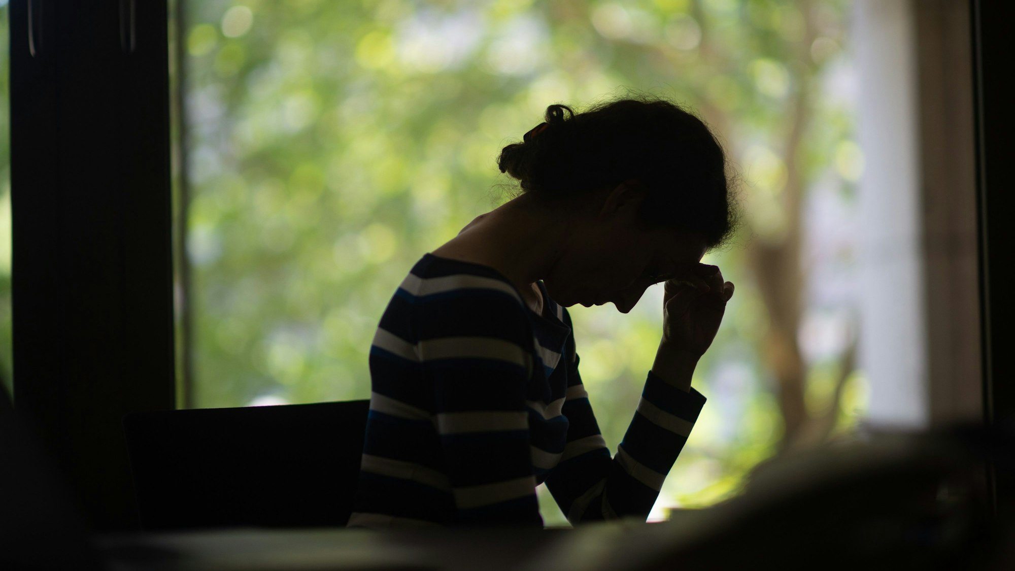 Eine Frau, von der man hauptsächlich die Silhouette erkennt, senkt den Kopf. (Symbolbild)