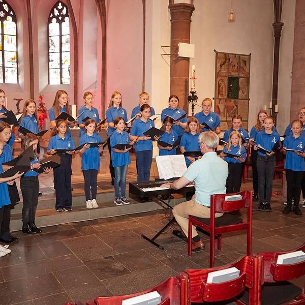 Der Mädchenchor aus Kevelaer steht im Altarraum der Marmagener Kirche und singt. Der Leiter Romano Giefer sitzt davor an einem Keyboard.