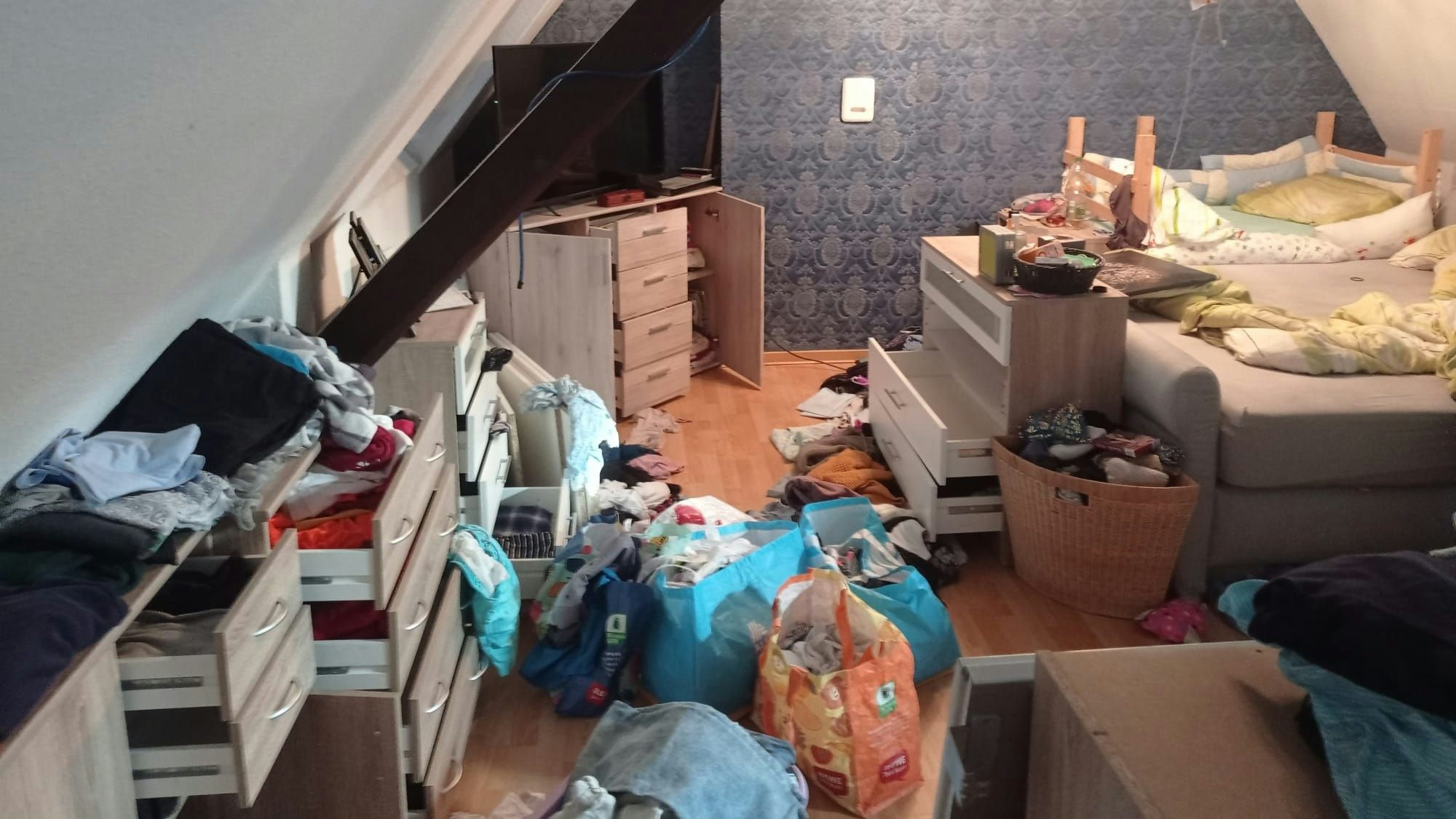 Das Foto zeigt ein durchwühltes Zimmer. Schubläden sind aufgerissen, Schranktüren geöffnet. Auf dem Boden liegen Gegenstände verstreut.