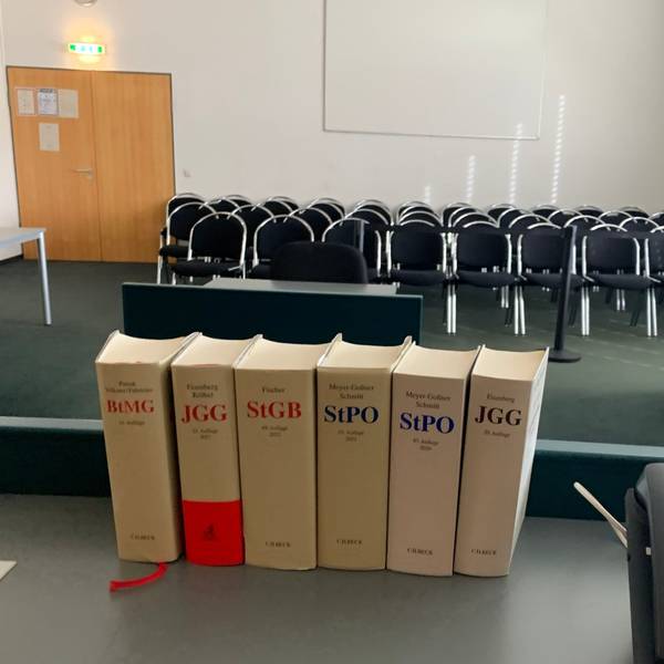 Das Symbolbild zeigt einen Gerichtssaal und im Vordergrund Bücher mit Gesetzestexten.