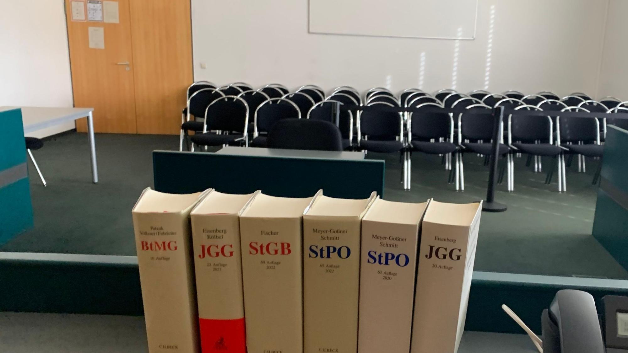 Das Symbolbild zeigt einen Gerichtssaal, im Vordergrund Bücher mit Gesetzestexten.