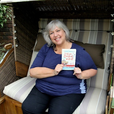 Eine Frau sitzt in einem Strandkorb und hält ein Buch in der Hand.