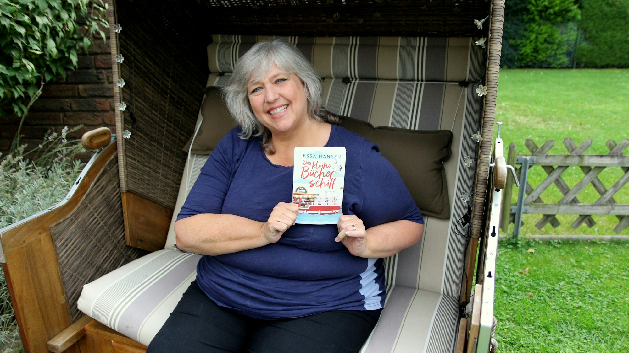 Eine Frau sitzt in einem Strandkorb und hält ein Buch in der Hand.