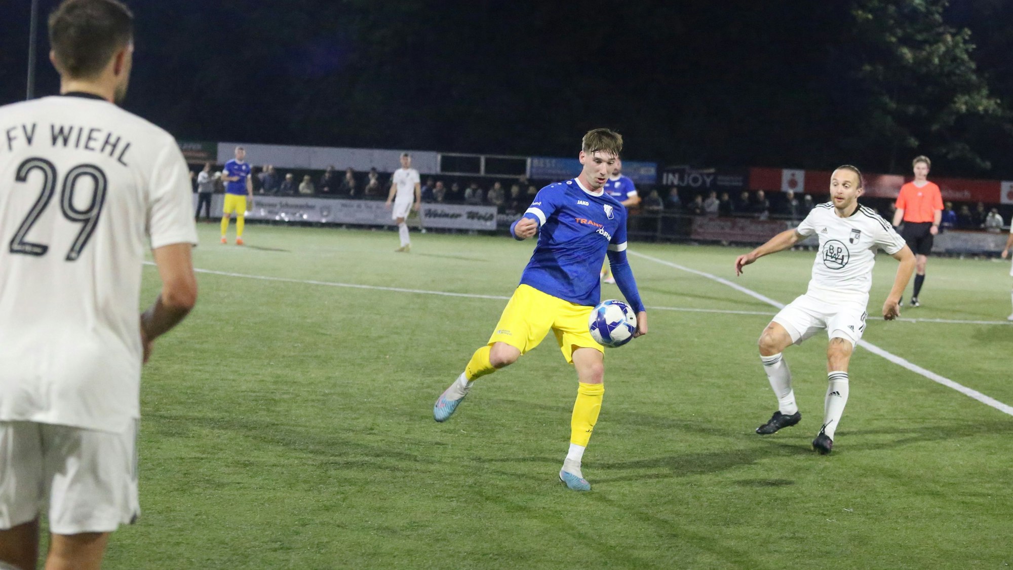 Flankiert von  zwei Wiehler Fußballern schießt ein Nümbrechter den Ball nach vorne.