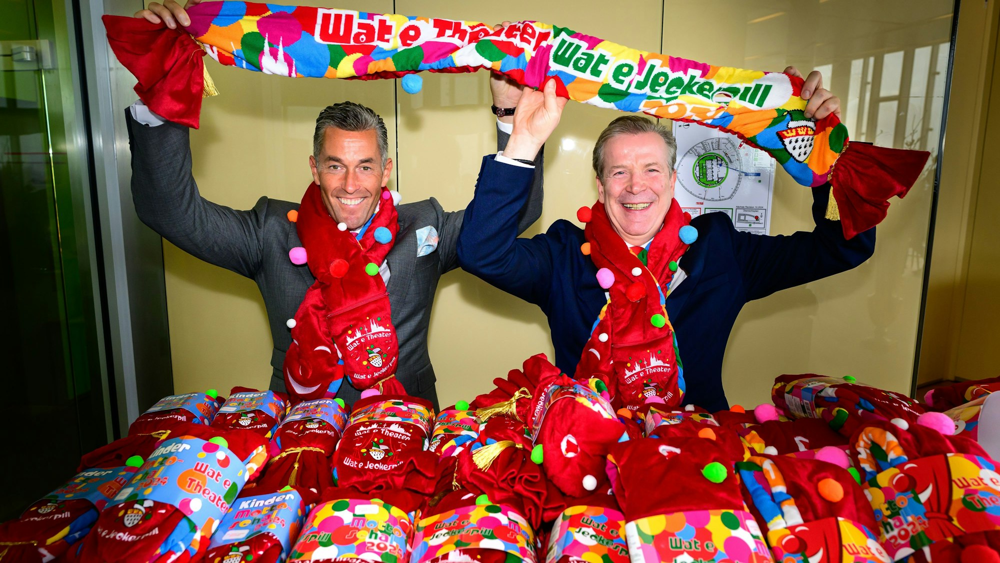 Der Mottoschal der Session 2024: Festkomitee-Präsident Christoph Kuckelkorn (r.) und Deiters-Chef Herbert Geiss präsentieren den Schal, der auf einer Seite einem Theatervorhang ähnelt.