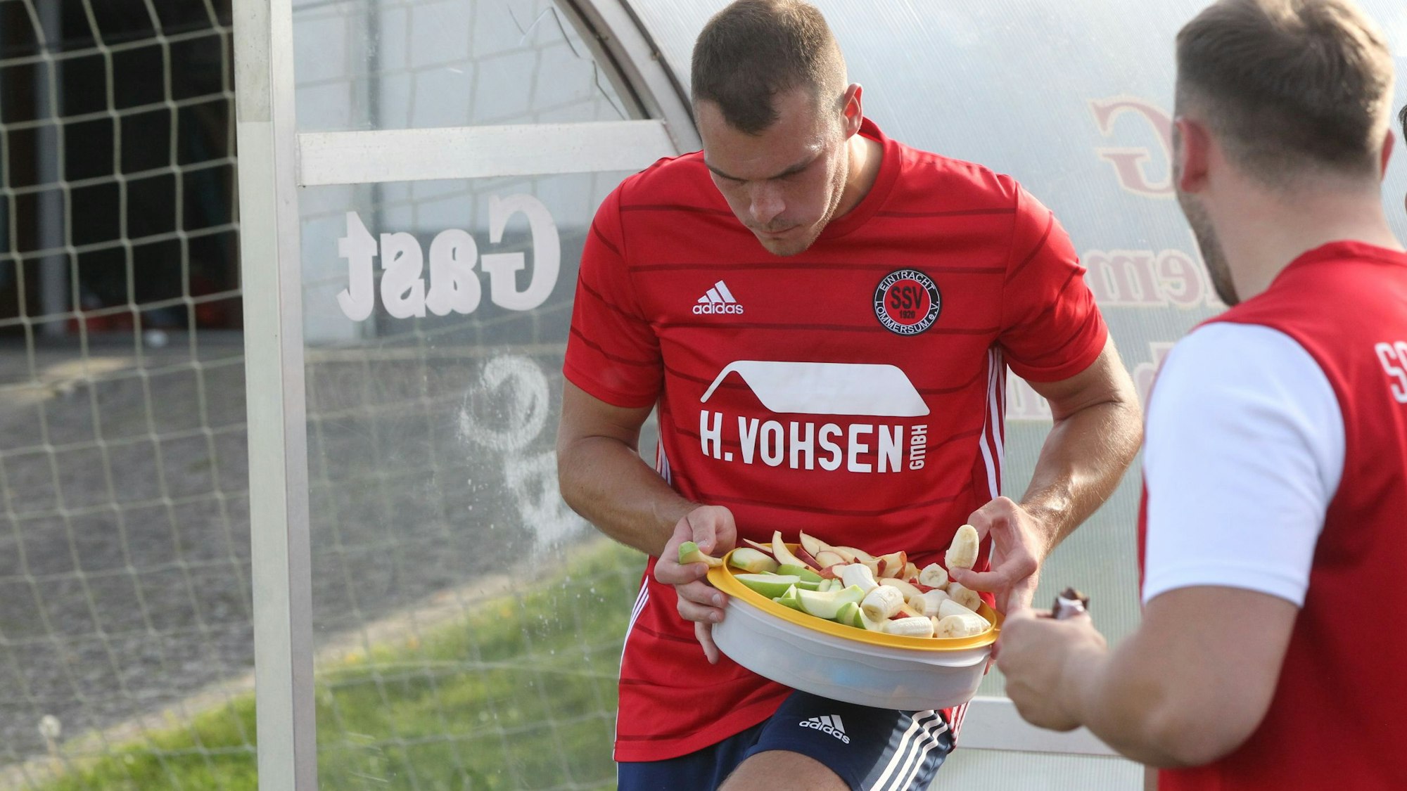 Das Bild zeigt zwei Fußballer des SSV Lommersum, wie sie Obst essen – und einen Schokoriegel.